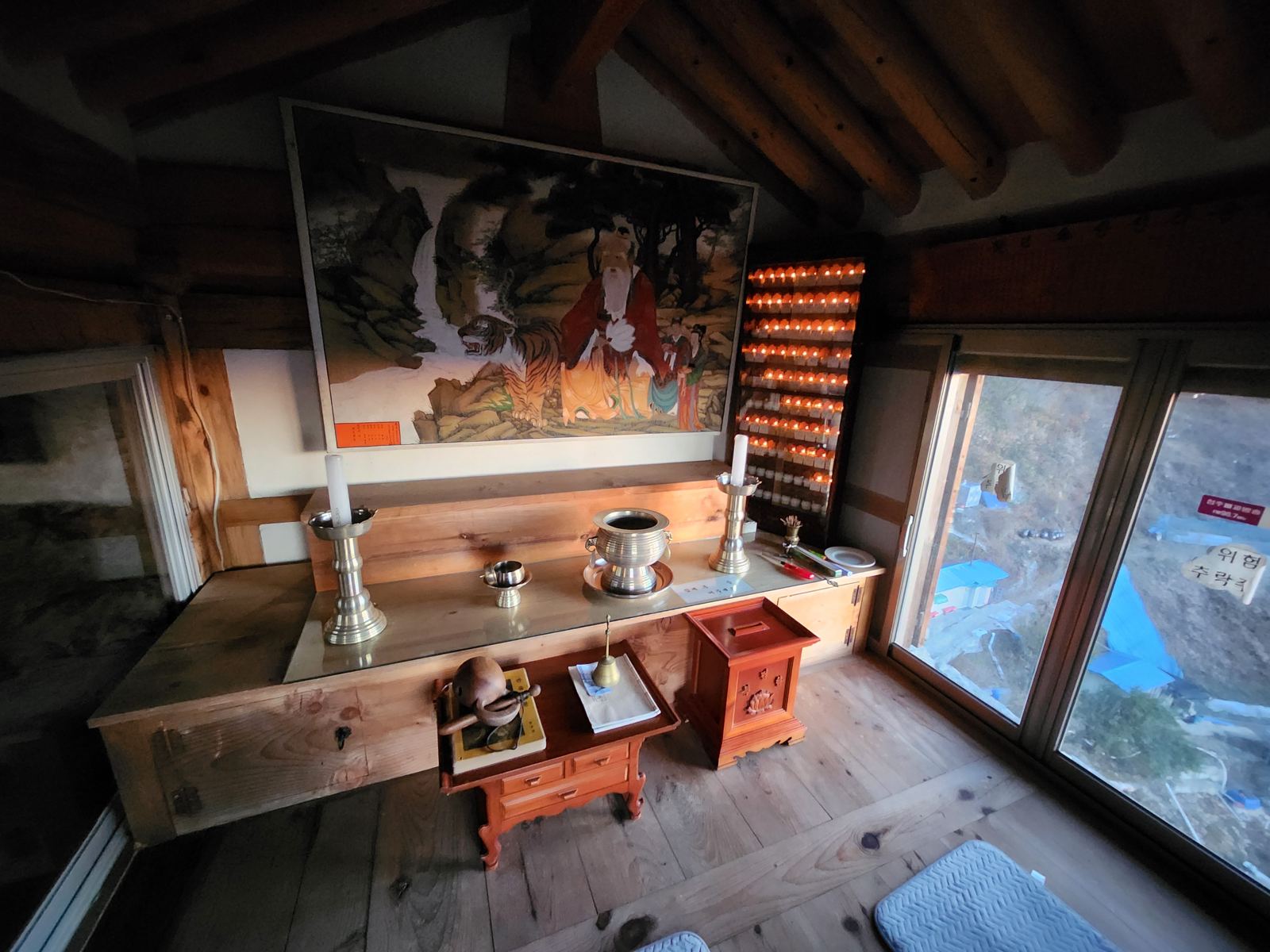 Inside the small shrine: a painting of the mountain spirit with a tiger above a wooden altar with brass candlesticks, prayer lamps glowing to the side