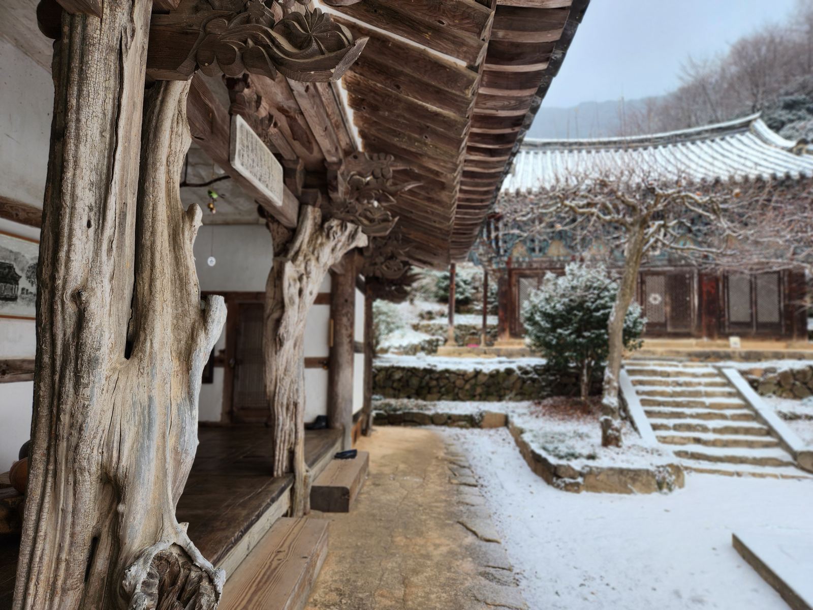 Quince-tree pillars and carved brackets beneath the eaves, with a snowy courtyard and painted hall beyond