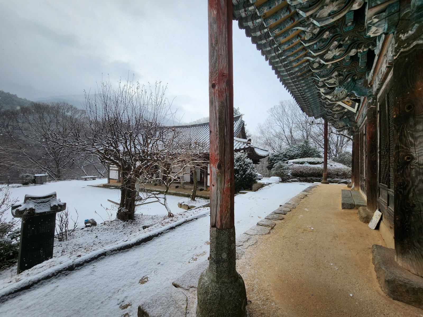 Painted eaves of a temple hall on the right, a snowy courtyard and bare trees on the left