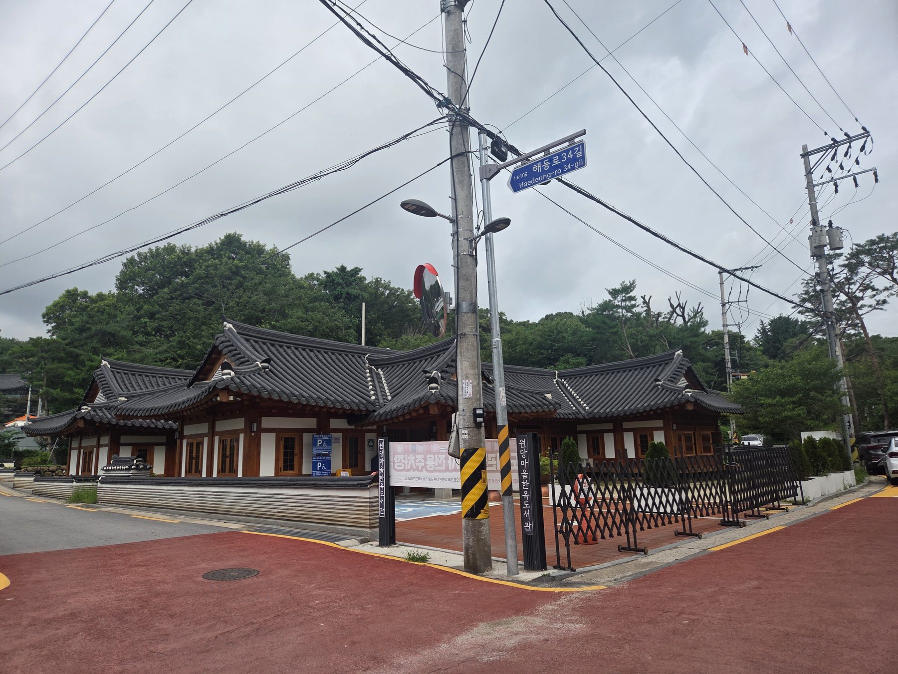 The tiled roofs of Wondang Village Hanok Library on a street corner, with a wooded hill behind
