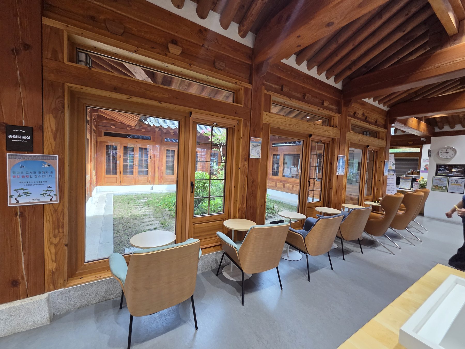 A row of armchairs and round tables along tall windows looking into the courtyard