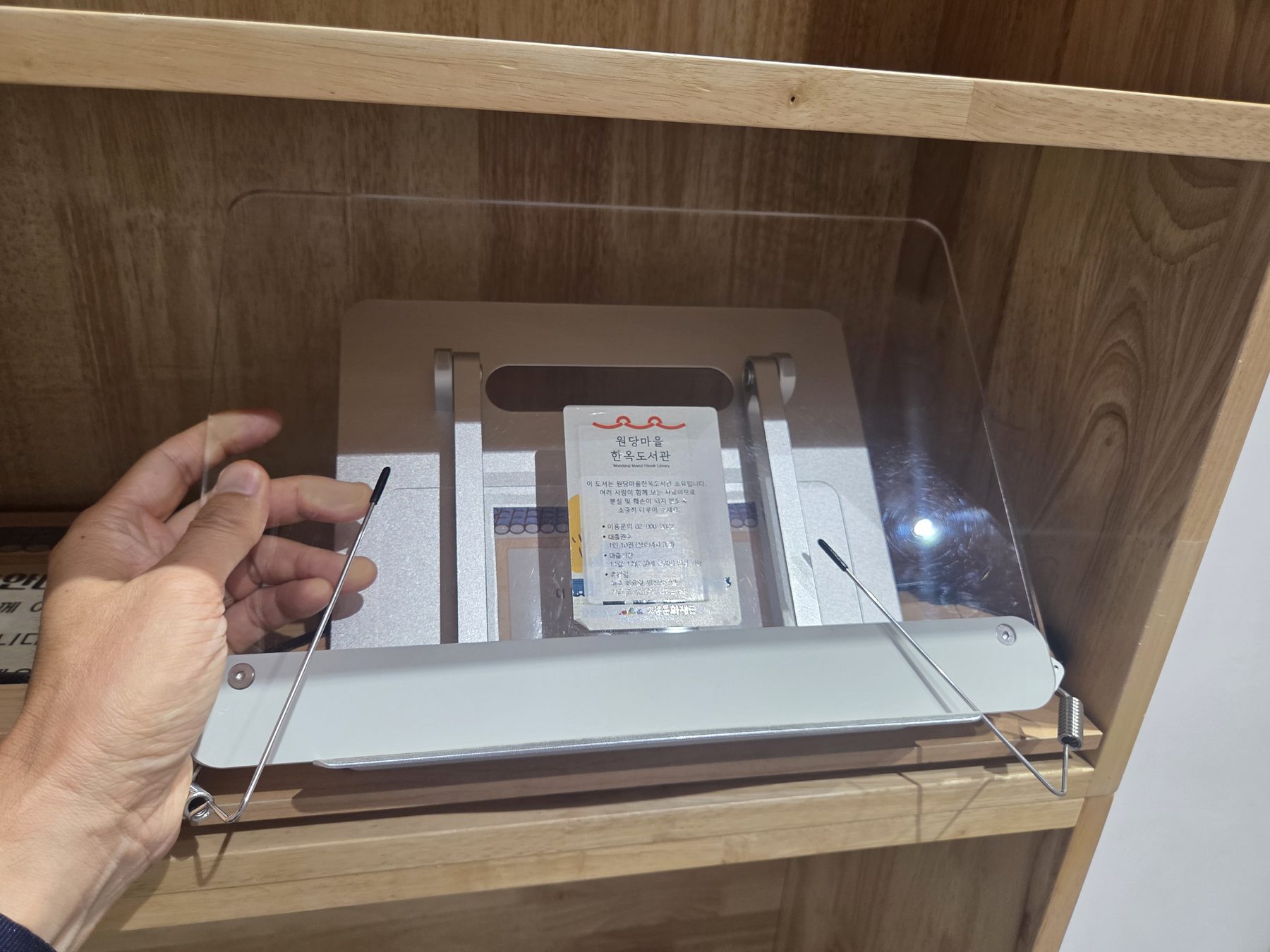 A metal book stand with a clear acrylic page holder, labelled as library property