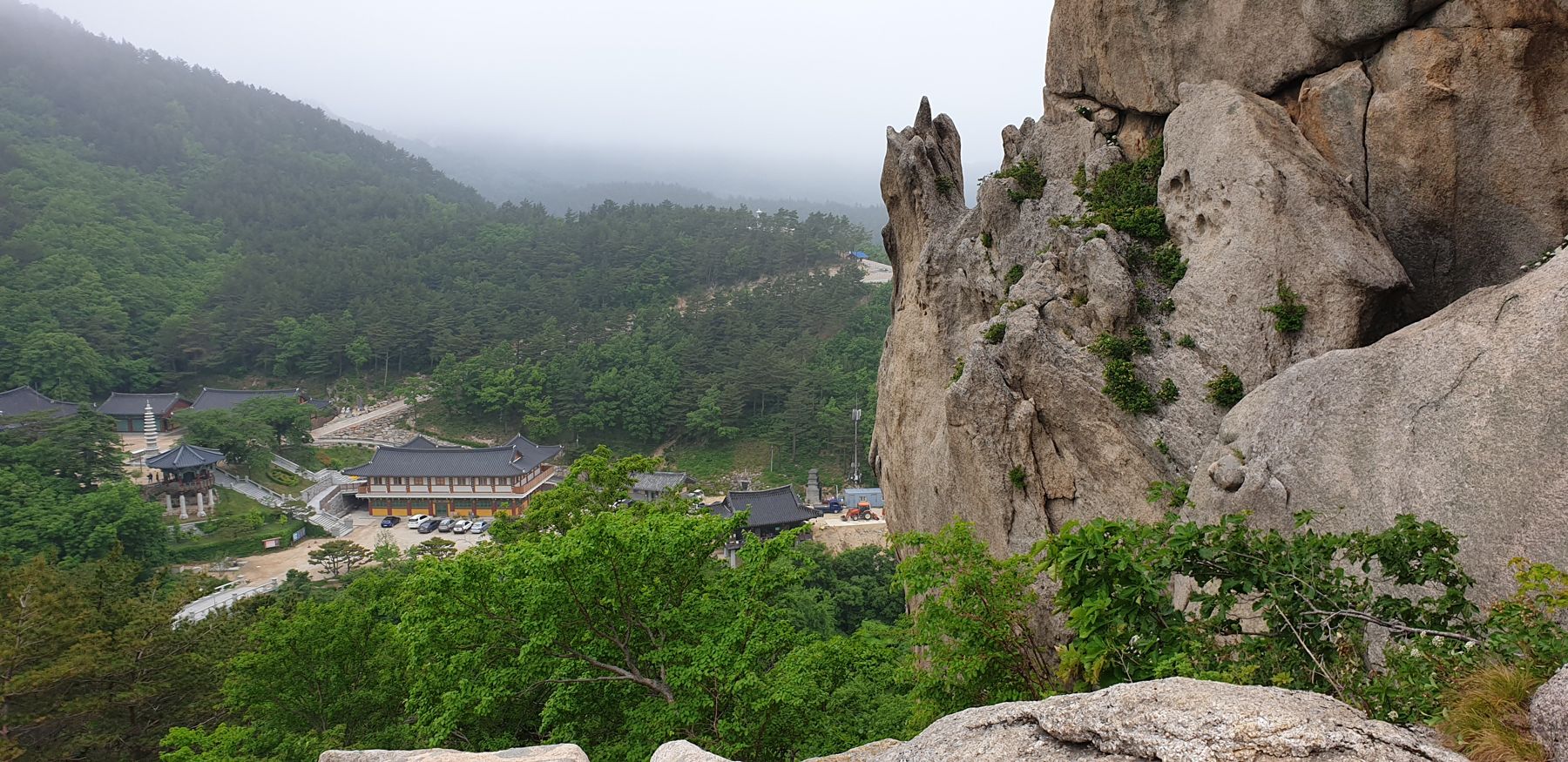 Hwaamsa's tiled roofs and pagoda seen from beside the Subawi boulder, with misty forested hills