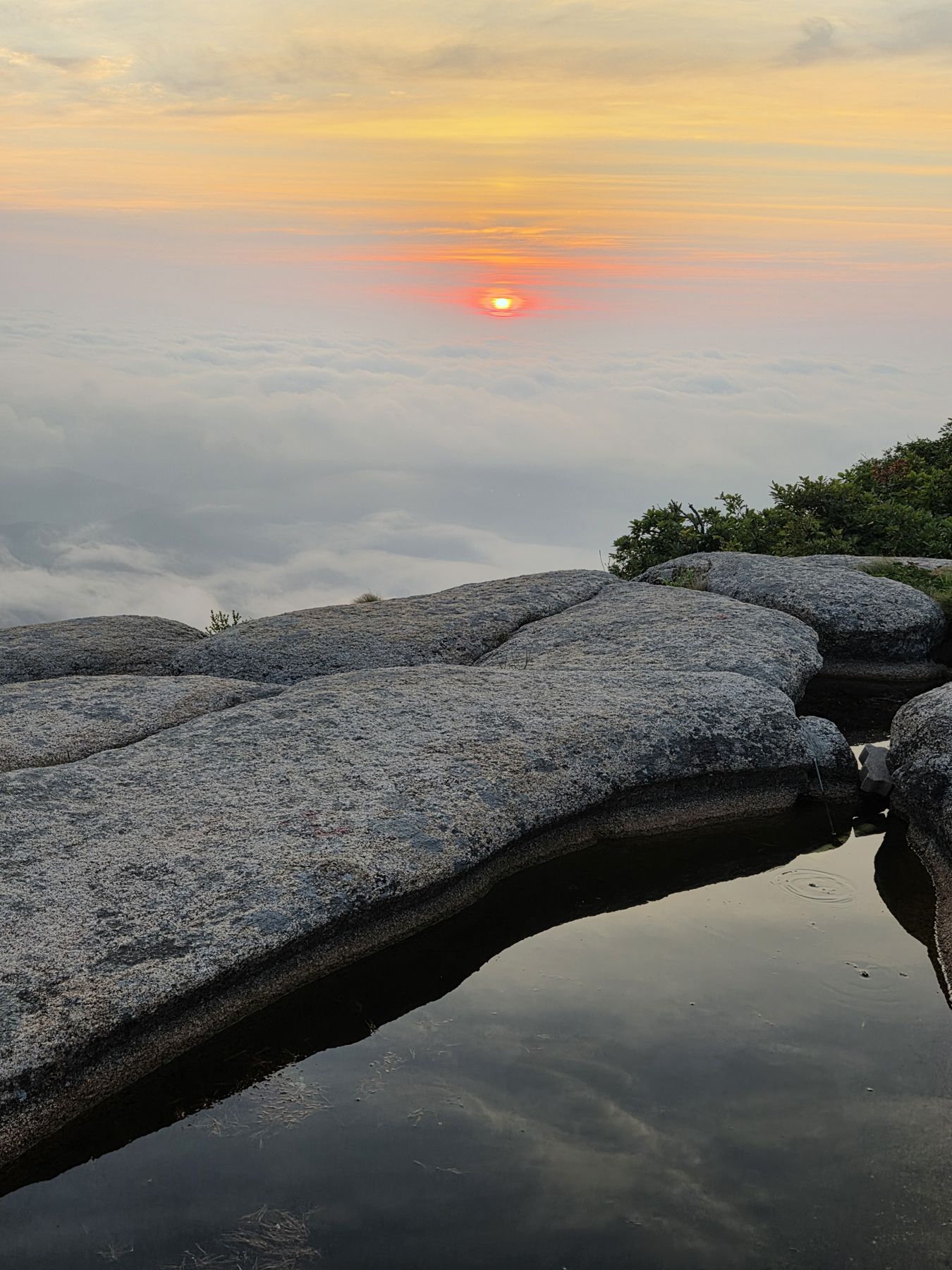 Red sun rising over clouds, reflected near a still rain pool in the granite